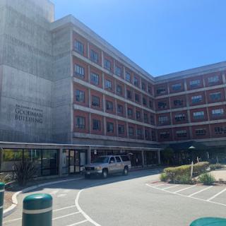 A modern multi-story building with a parking area, captured in bright daylight.