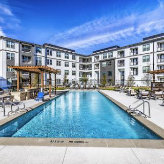 A beautiful modern apartment complex featuring a sparkling swimming pool under a clear blue sky.