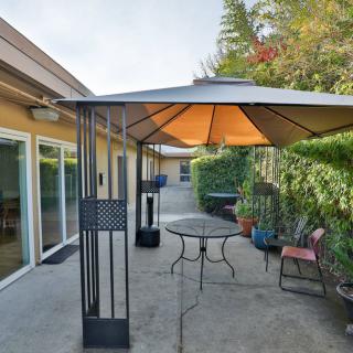 A cozy outdoor patio with a gazebo, table, and chairs, surrounded by a lush hedge.