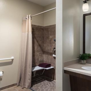 An accessible bathroom with a tiled shower area, curtain, and sink.