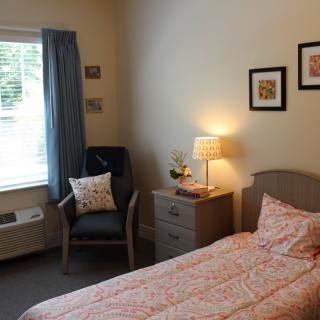 Cozy bedroom with a single bed, bedside table, and comfortable chair by the window.