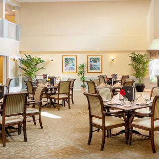 A well-lit dining room with neatly arranged tables and chairs, featuring elegant decor and green plants.