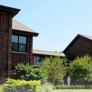 A suburban brick house with landscaped greenery and trees.
