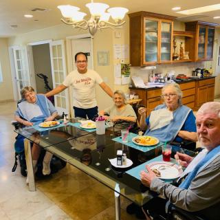 A group of people gathered around a table enjoying a meal together in a kitchen setting.