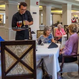 A waiter serves drinks to a group of customers seated at a restaurant table.