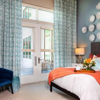 A stylish bedroom interior with a colorful bed, decorative curtains, and modern wall art.