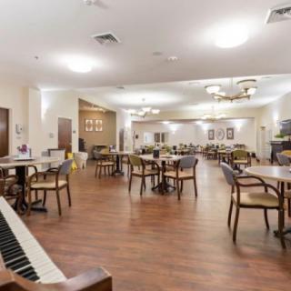 A spacious dining area with empty tables and chairs, featuring a piano and elegant chandeliers.