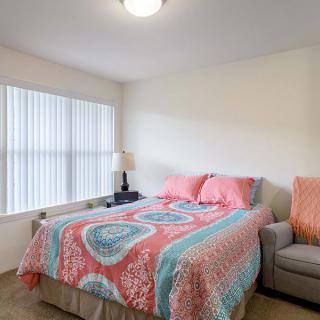 A cozy bedroom featuring a colorful bedspread, a cushy couch, and ample natural light through large windows.