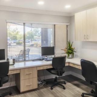 A modern office space featuring two workstations with computers, ergonomic chairs, and a large window with blinds.