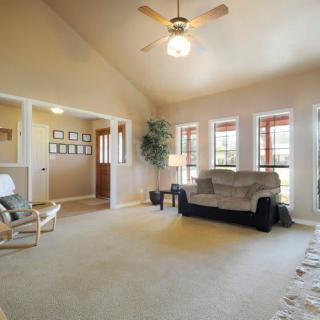 Spacious living room with a comfortable sofa, large windows, and ceiling fan.