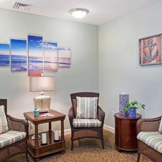 A cozy waiting room with comfortable chairs, a lamp, and decorative artwork on the walls.