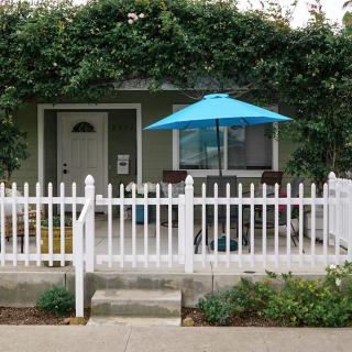 A cozy house with a white picket fence and outdoor patio under a blue umbrella.