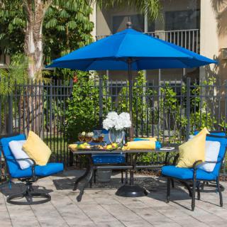 A cozy outdoor patio setup featuring blue and yellow cushioned chairs with a matching blue umbrella.