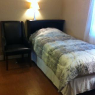 A cozy bedroom with a single bed, a chair, and a wall-mounted lamp.