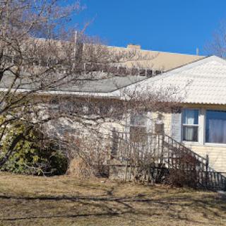A modest residential house with a tree in the front yard, set against a clear blue sky.