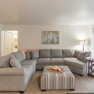 A cozy living room with a gray sectional sofa and striped ottoman, complemented by soft lighting and wall art.