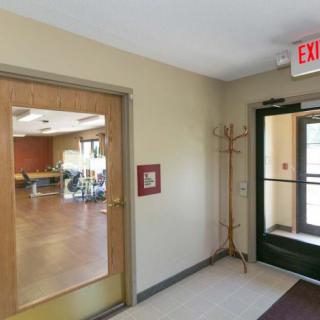 A hallway with a glass door leading to another room, featuring an exit sign and coat rack.