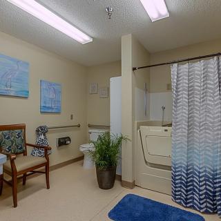 A well-lit, accessible bathroom with a walk-in bathtub, chair, and blue-themed decor.