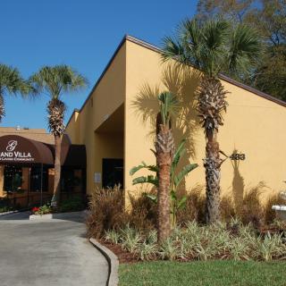 A restaurant with a yellow exterior and palm trees in front, featuring an awning over the entrance.