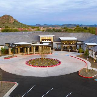 A modern building with a circular driveway surrounded by desert landscape and mountains in the background.