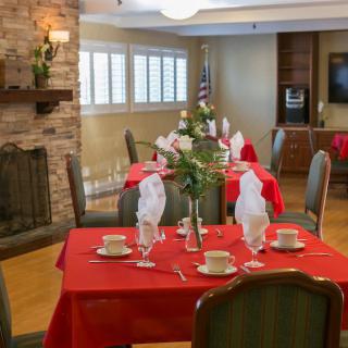 A warmly decorated dining room with tables set for a formal meal, featuring red tablecloths and neatly arranged napkins.