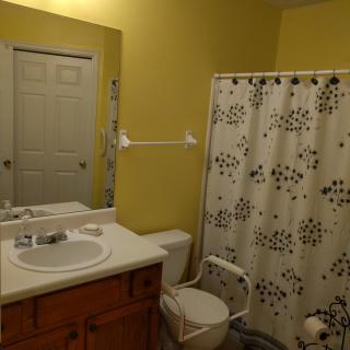A bathroom with yellow walls, featuring a sink, mirror, toilet, and a shower with a patterned curtain.