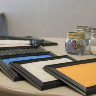 A collection of framed sand art pieces alongside jars filled with colorful sand.
