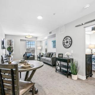 A modern living and dining area with neutral tones, featuring a wall clock and indoor plants.