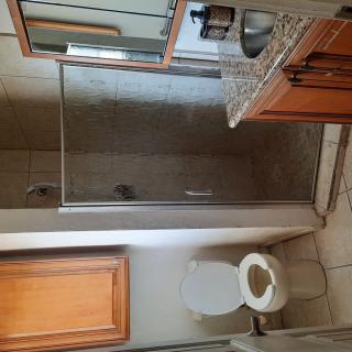 A clean bathroom featuring a toilet, sink, mirror, shower, and wooden cabinetry.