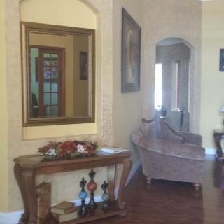 A cozy living room featuring a mirror above a wooden table, with a sofa in the background.