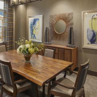 A modern dining room with a wooden table, surrounded by chairs, adorned with decorative artwork and a mirror on the walls.