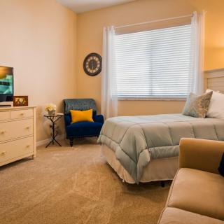 A cozy and well-decorated bedroom featuring a bed, armchair, dresser, and soft lighting.