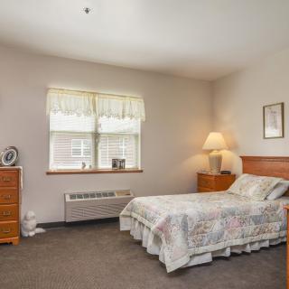 A cozy bedroom with a neatly made bed, dresser, and a lamp beside the window.