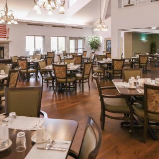 A spacious dining area with neatly arranged tables and chairs, featuring elegant chandeliers and a warm wooden floor.
