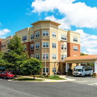 A residential apartment building with a driveway and parked vehicles under a blue sky with clouds.