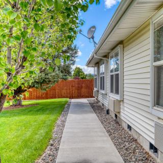A walkway alongside a house with a well-maintained lawn and wooden fence.