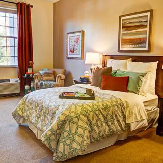A cozy bedroom with a neatly made bed, artwork on the walls, and warm lighting.