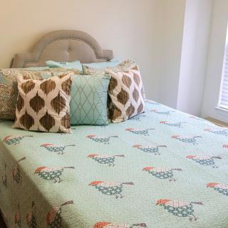A cozy bedroom with a bed featuring chicken-patterned bedding and decorative pillows.