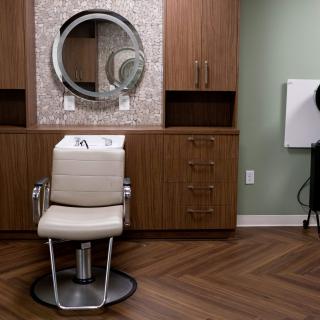 A stylish hair salon interior featuring a barber chair in front of a circular mirror and wooden cabinets.