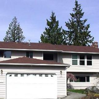 A suburban two-story house with a garage and surrounding trees.
