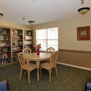 A cozy reading room with a round table surrounded by chairs, bookshelves filled with books, and a window letting in natural light.
