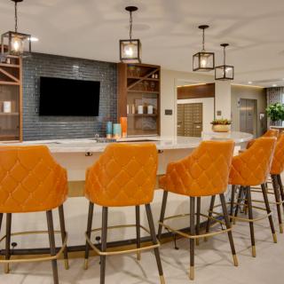 A modern kitchen with a large island, featuring orange bar stools and pendant lighting.