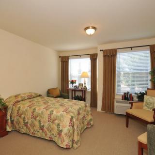 A cozy bedroom with a bed, two windows, and a small desk.