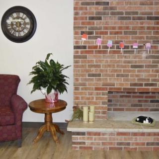 A cozy living room with a brick fireplace, an armchair, a side table with a plant, and decorative items.