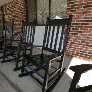 A row of black rocking chairs on a porch with a brick wall backdrop.