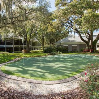 A serene garden scene featuring a well-maintained putting green surrounded by lush trees and landscaping.