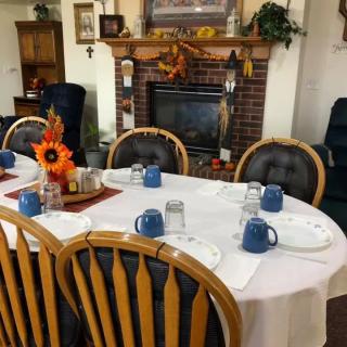 A cozy dining room with a table set for a meal, featuring fall-themed decorations and a fireplace in the background.