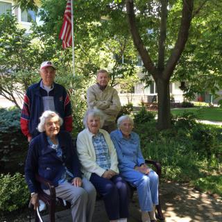 A group of elderly people sitting and standing together on a sunny day in a park.