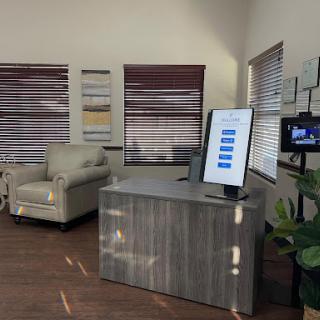 A modern office waiting area featuring a reception desk, digital display, comfortable seating, and stylish window treatments.