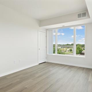 A bright, empty room with hardwood floors and a large window offering a scenic view.